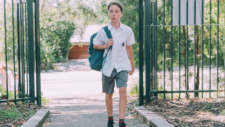 Male primary student walking into school with backpack.