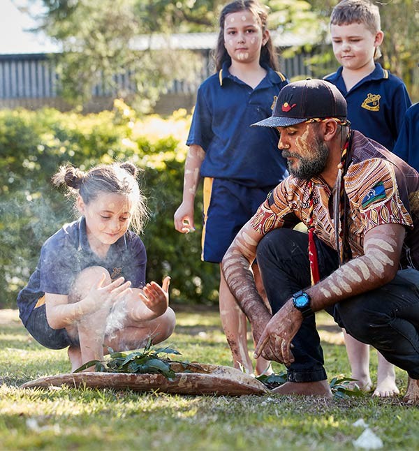 A young girl takes part in a smoking ceremony conducted by a young Aboriginal man.